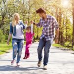 A happy family, young caucasian parents hiking with their daughter in a park on a beautiful sunny day