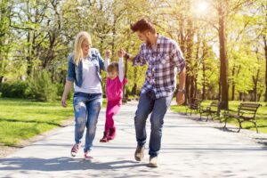 A happy family, young caucasian parents hiking with their daughter in a park on a beautiful sunny day