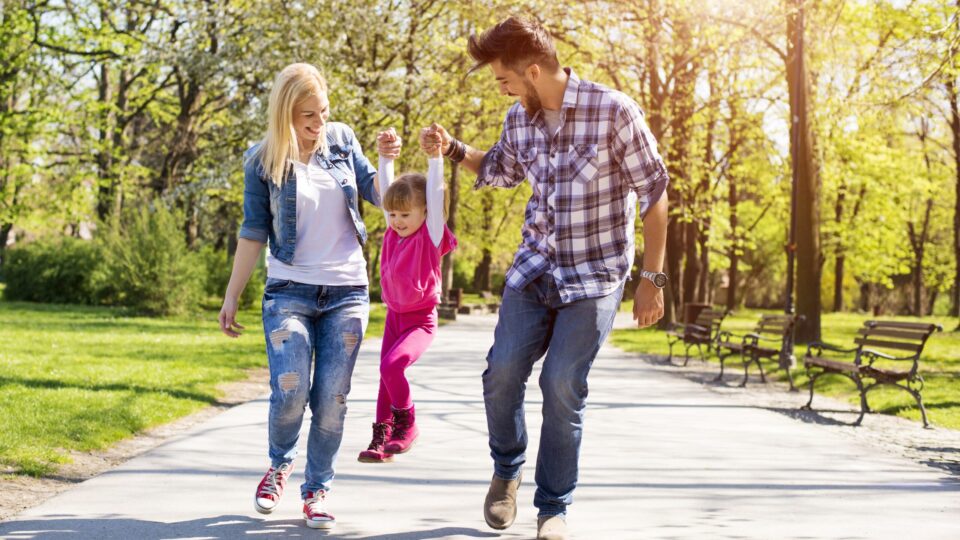 A happy family, young caucasian parents hiking with their daughter in a park on a beautiful sunny day