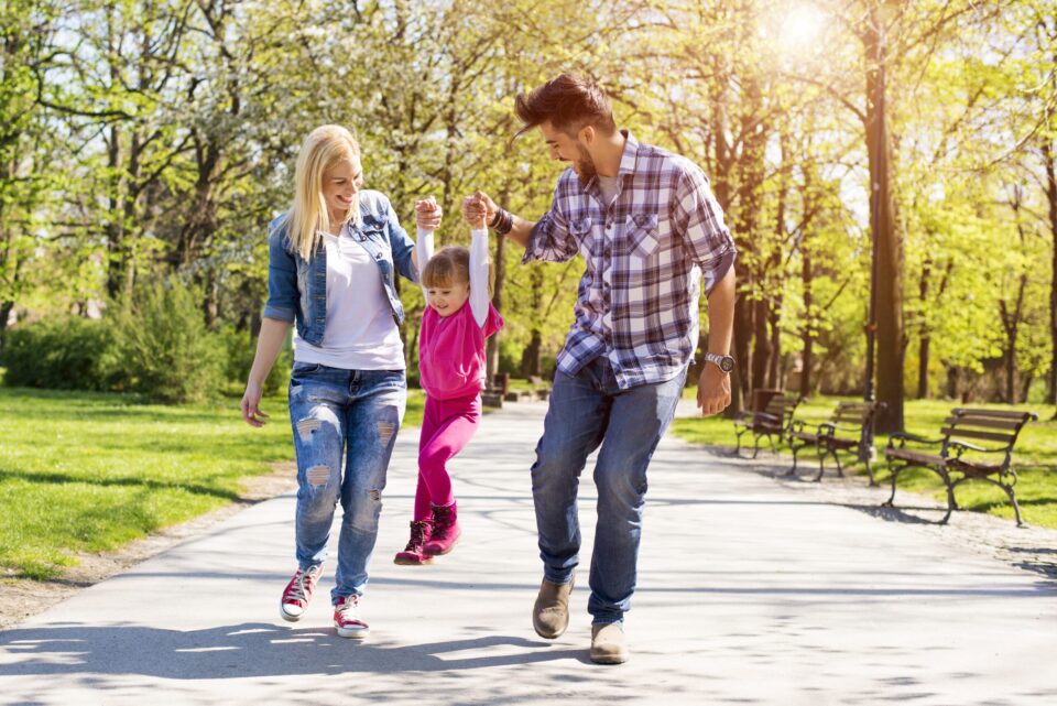 A happy family, young caucasian parents hiking with their daughter in a park on a beautiful sunny day